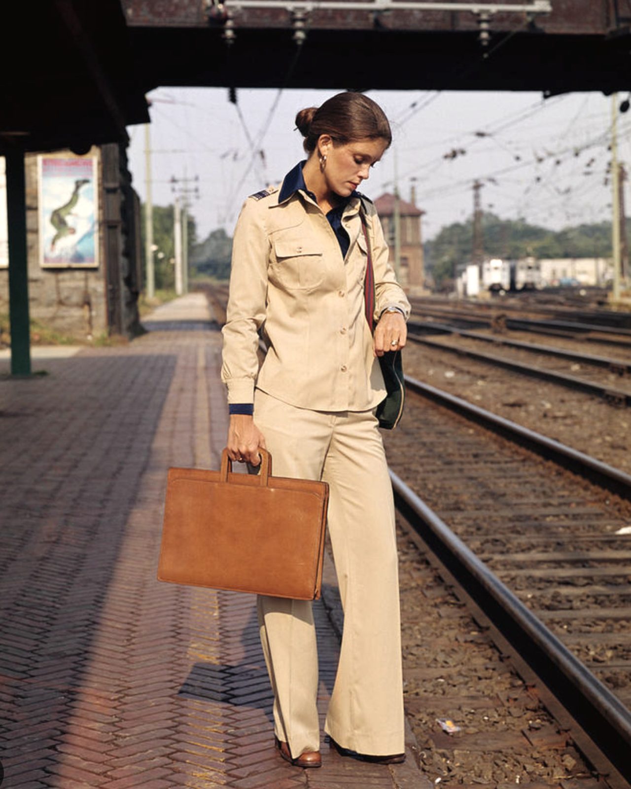 a woman in a tan suit with a leather portfolio on a train platform, 1970s